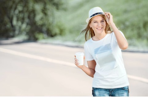Beautiful young woman walking with a disposable coffee cup, drinking coffee and smiling against the