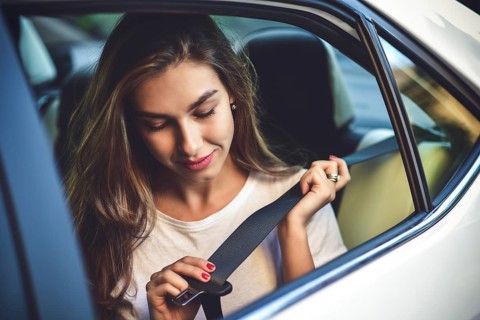 Beautiful woman with phone smiling while sitting on the back seat in the car