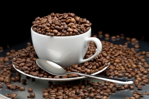 Cup and saucer full of coffee beans with a spoon on a black background