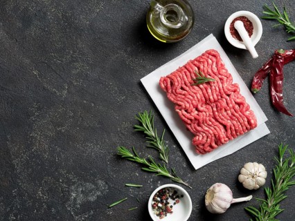Fresh raw minced beef on backing paper and cutting board and ingredients over black cement