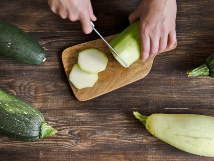 Zucchini harvest. Woman slices zucchini on wooden table. Farm organic zucchini harvesting