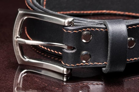 Black leather belt with a metal buckle on a dark background close-up