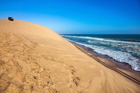 Ocean surf with foamy waves. Atlantic coast of Walvis Bay, Namibia, south of Africa. Dangerous jeep