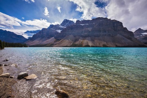 The cold waters of the lake surrounded by scenic Canadian Rocky Mountains. Azure Bow Lake in Banff