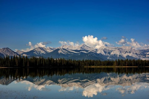 The Canadian Rockies and bright blue sky are reflected in a lake near Canmore, Alberta, Canada,