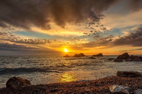 Dramatic sunset sky over beach rocks and waves, Adriatic Sea