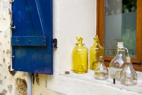 Still life with old glass bottles in window with blue shutters in France