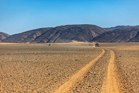 Dusty desert road leads through barren landscape with mountains, By off-road vehicle through the