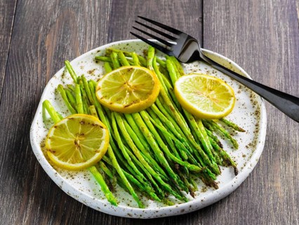 Close up view of grilled asparagus and slice of lemon in craft trendy plate on brown wooden table