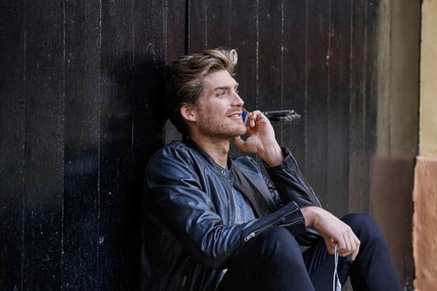 Young man with smartphone earphones sitting in the street black door