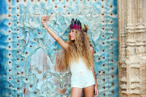 Blond teen girl tourist in Mediterranean old town door with colorful feathers on hair