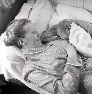 1950s mother nursing her baby. A young woman breastfeeding her baby while lying in bed at home.