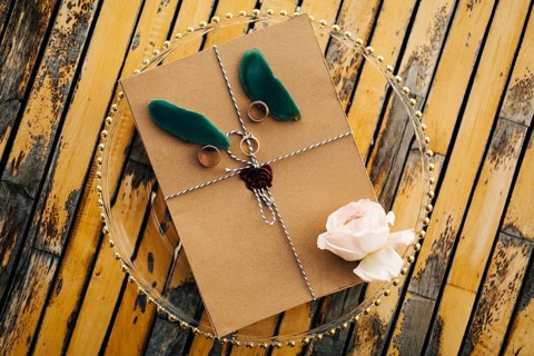 Beautiful brown envelope tied with a rope with rings, a rose and petals lies on a transparent tray