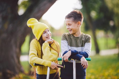 Twins 10 years old in bright clothes spend time actively together in autumn park riding kick