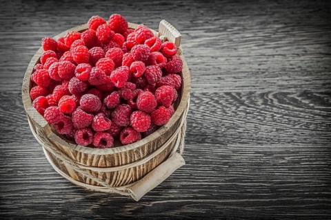 Red raspberry in bucket on vintage wooden board