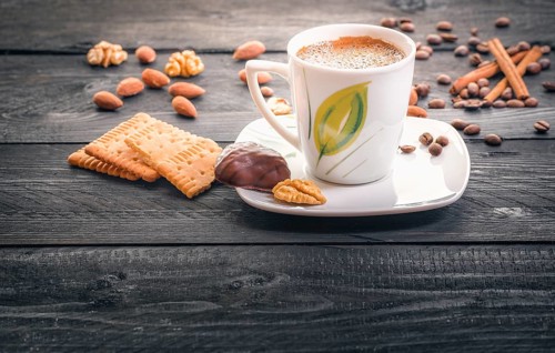 Cup of hot coffee on a plate, surrounded by tasty and healthy snacks, biscuits, almonds, walnuts