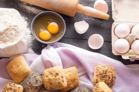 High angle view with a bag of flour, eggs, a rolling pin and freshly baked bread rolls, decorated