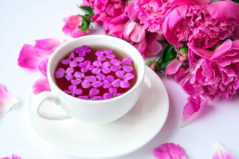 Creative layout with pink peonies flowers and cup of tea on bright table. Spring Seasonal