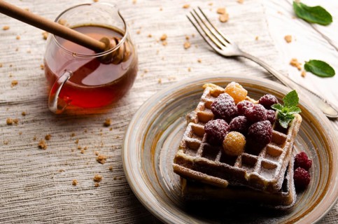 Belgian waffles served with raspberries and mint leaf dusted with powdered sugar on white wooden