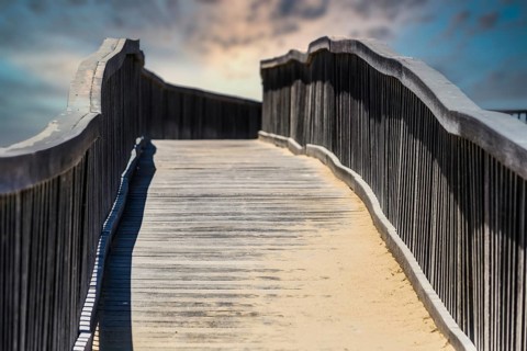 Wooden walkway bridge covered with sand, leading to infinity point