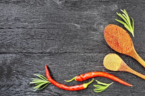 Frame of sprigs of fresh rosemary, pods of red hot pepper and two spoons with ground pepper on a