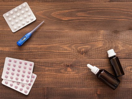 Medications or tablets and drops and electronic thermometer on a dark wooden background with copy