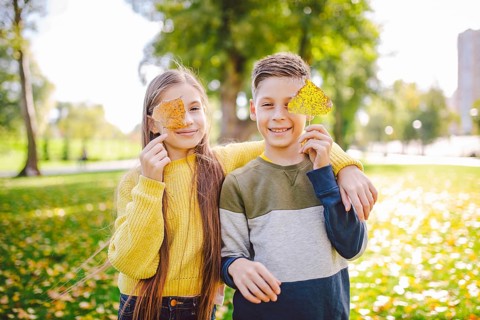 Happy Caucasian siblings enjoying in autumn day in park, sunny weather. Kids having fun holding