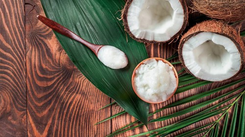 Top view of coconut MCT oil in bowl and in spoon and halved coco-nut on wooden table. Health
