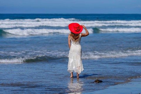 Breathtaking woman basks in beach bliss, near a pier, under clear blue skies, embracing the