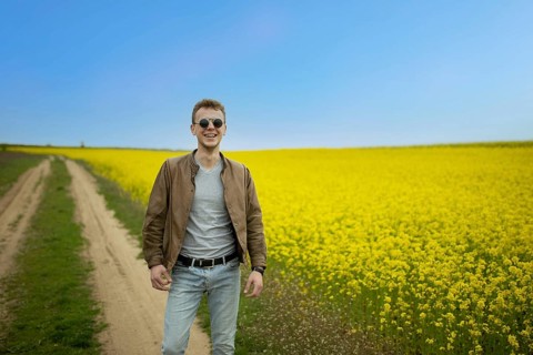 Man in sunglasses stands happily in a field of yellow flowers under a clear blue sky