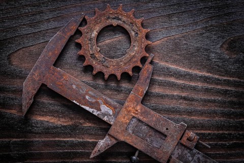 Rusted age-old measuring calipers with gear wheel on vintage dark wooden background construction