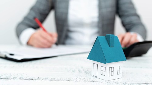 Businesswoman sitting and writing in notebook. Paper house' on desk