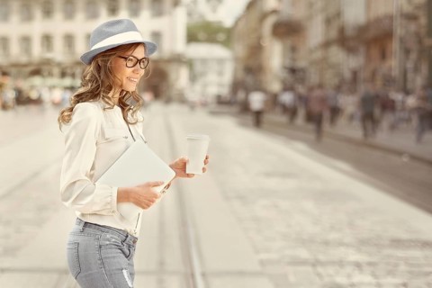 Beautiful young woman with a disposable coffee cup drinking coffee, holding a tablet in her hands