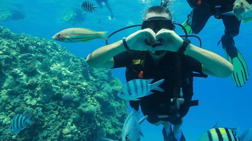 Scuba diver makes heart with his hands underwater during scuba diving at coral reef