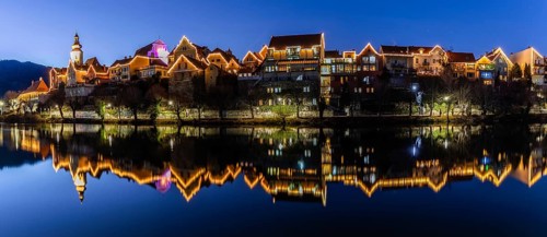 Christmas illuminated house facade of Frohnleiten reflected in the river Mur, panoramic shot, blue