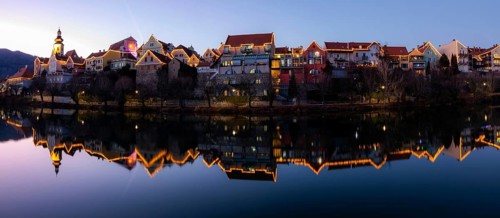 Christmas illuminated house facade of Frohnleiten reflected in the river Mur, panoramic shot, blue