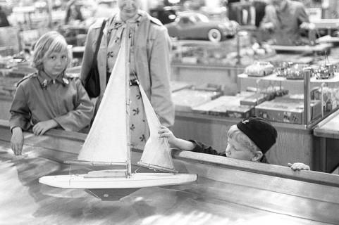 Toys in the 1950s. At a department store a boy is curious of the nice sailboat model floating in