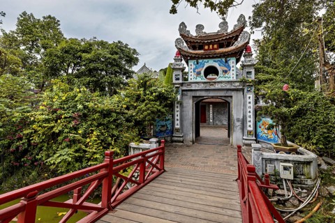 A richly decorated temple with a wooden walkway, surrounded by lush greenery and Asian