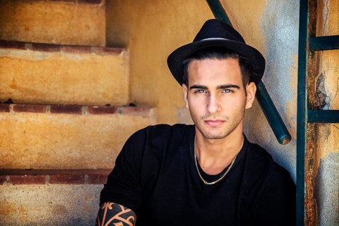 Portrait of handsome man with tattoo on hands sitting on cement stairs while leaning on wall