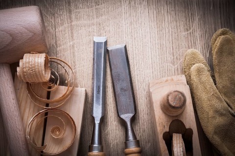 Wooden bricks mallet curled up shavings planer firmer chisels leather gloves on wood background