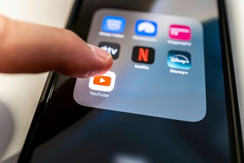 One finger touches the YouTube icon on a smartphone screen with various other streaming apps
