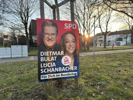SPD election poster with two politicians, in the background a quiet city scene at sunset, election