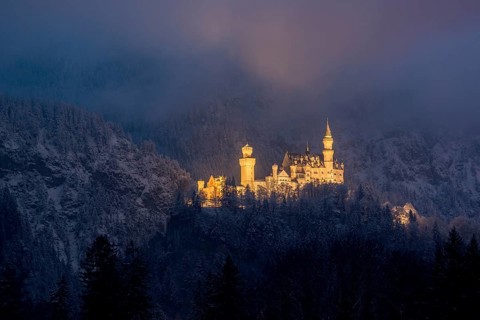 A mysteriously illuminated castle rises above a snow-covered forest in the evening mist,