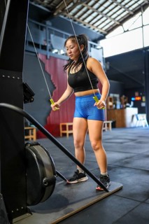 Vertical photo of a strong Chinese woman exercising with weights in a lat pulldown machine