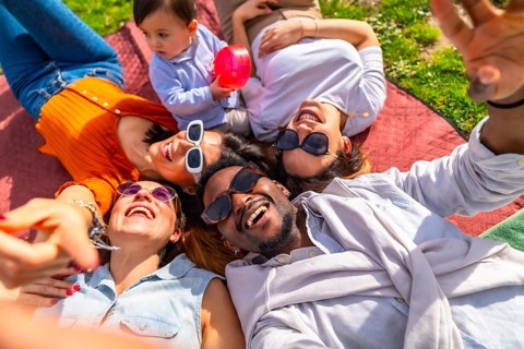 Group of cheerful multi ethnic friends taking a selfie while lying in a circle on a blanket at the