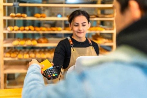 Rear view of a latin man paying with credit card and contact less terminal in an artisan bakery