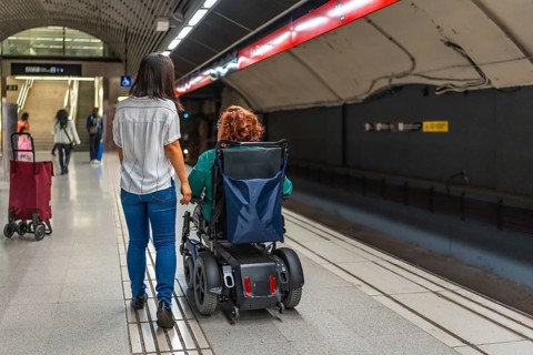 Rear view of a disabled caucasian adult woman in wheelchair and asian friend walking along metro