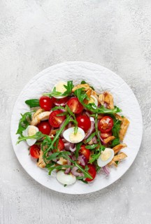 A warm salad with fried chicken fillet, arugula and cherry tomatoes, and boiled quail eggs, on a