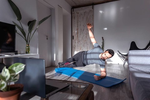 Latin man at home training side plank. Online training class