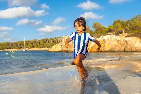 Happy child running on the wet sand of s'amarador beach in mallorca, spain, during summer holidays,